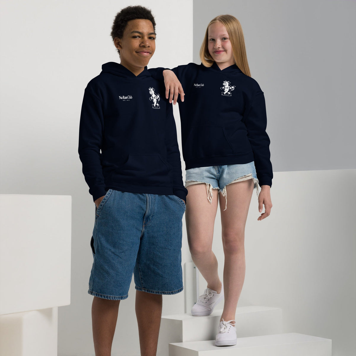 Two children wearing navy blue hoodies with a logo, standing on white steps.
