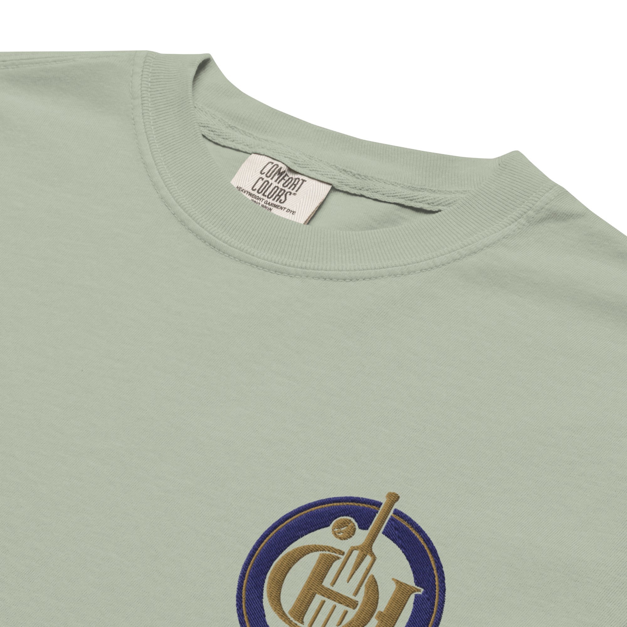 Close-up of a sage green t-shirt  and a small circular graphic on the chest featuring a gold and blue design.