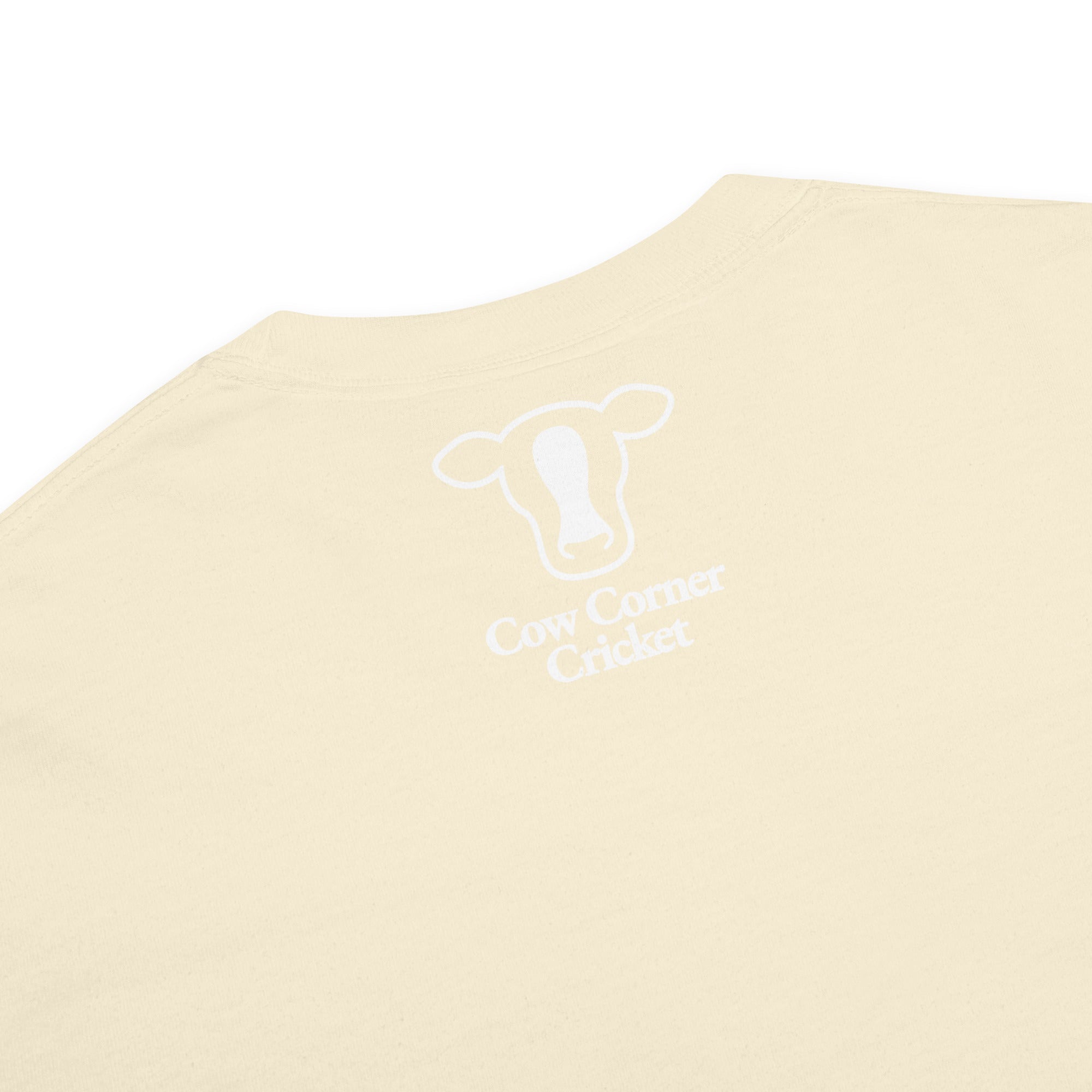 A close-up of a cream-colored t-shirt  and a white graphic print of a cow head outline with the text 'Cow Corner Cricket' underneath.