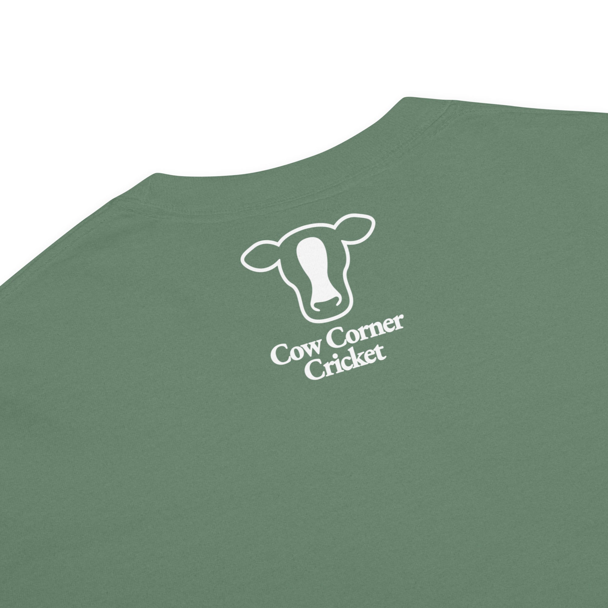 A close-up of  green t-shirt featuring a white graphic of a cow head outline above the text 'Cow Corner Cricket'.