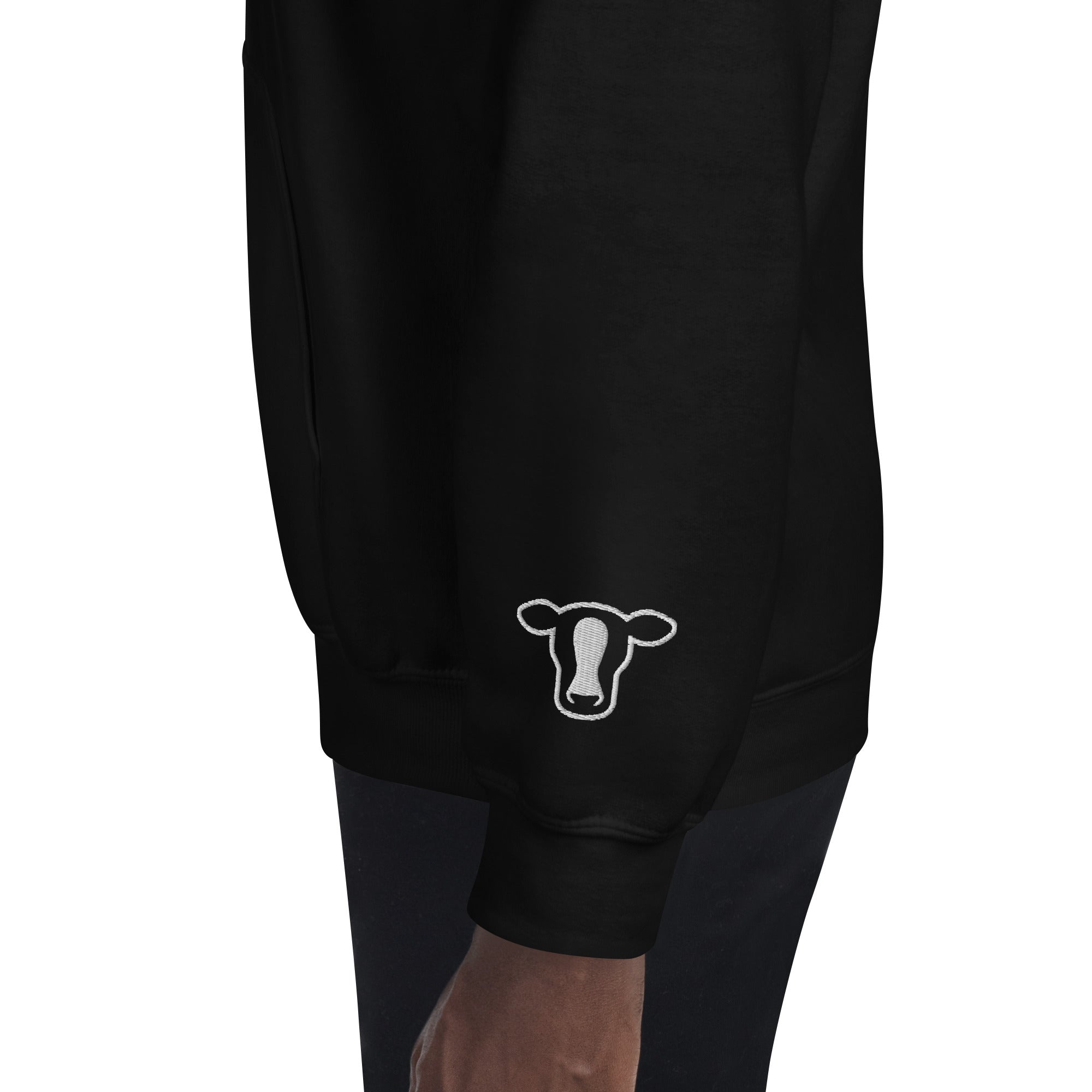 Black sweatshirt worn by a model, featuring a white line-art cow head graphic on the lower left sleeve