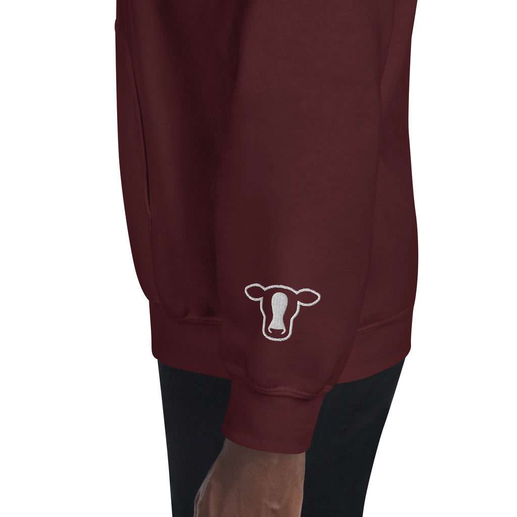A close-up of a maroon sweatshirt worn by a model, featuring a white outline cow graphic on the lower left sleeve.