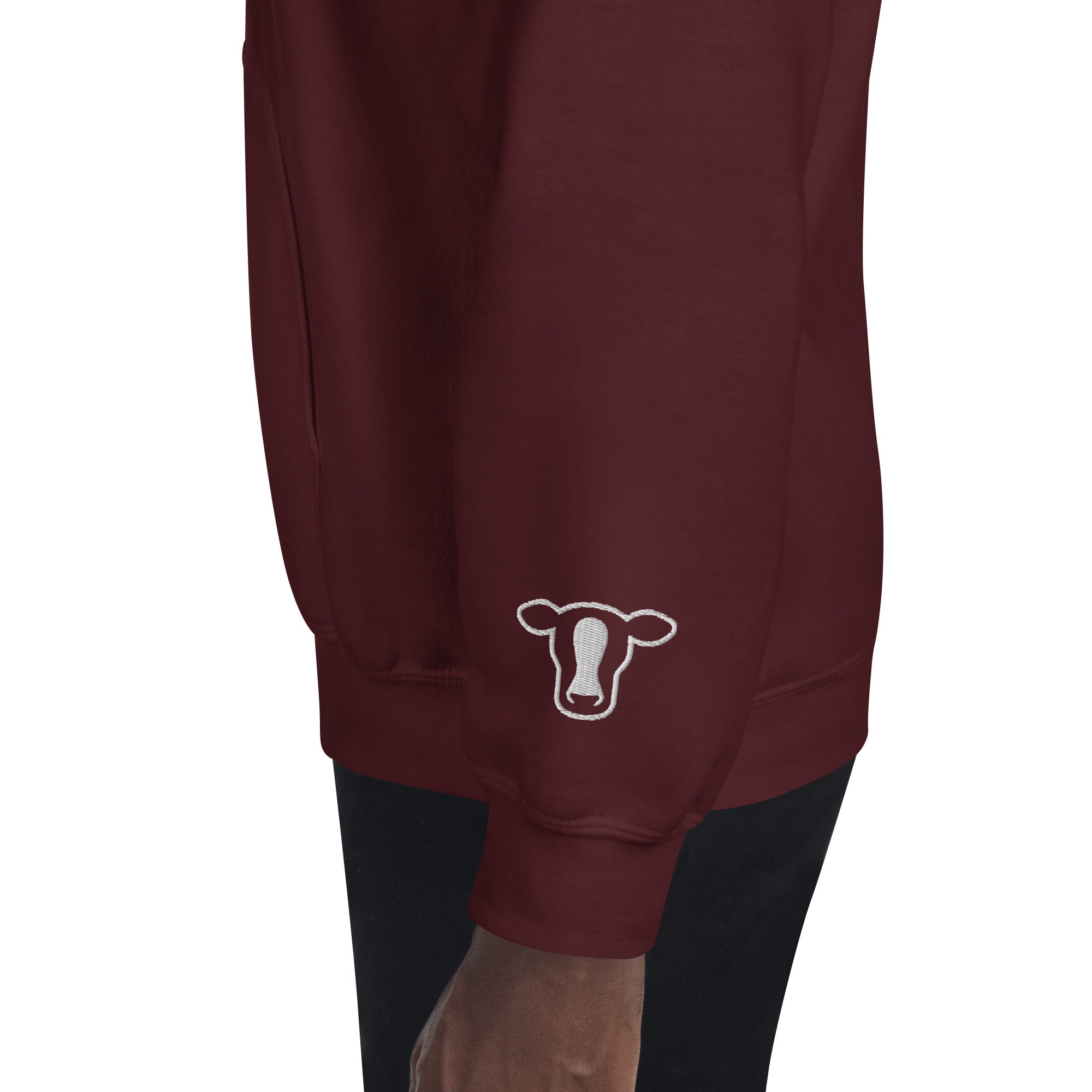 A close-up of a maroon sweatshirt worn by a model, featuring a white outline cow graphic on the lower left sleeve.