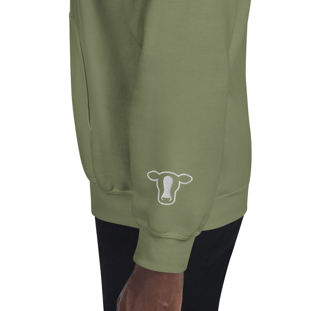 Close-up of a person wearing green sweatshirt with a white cow outline graphic on the left sleeve, paired with black pants