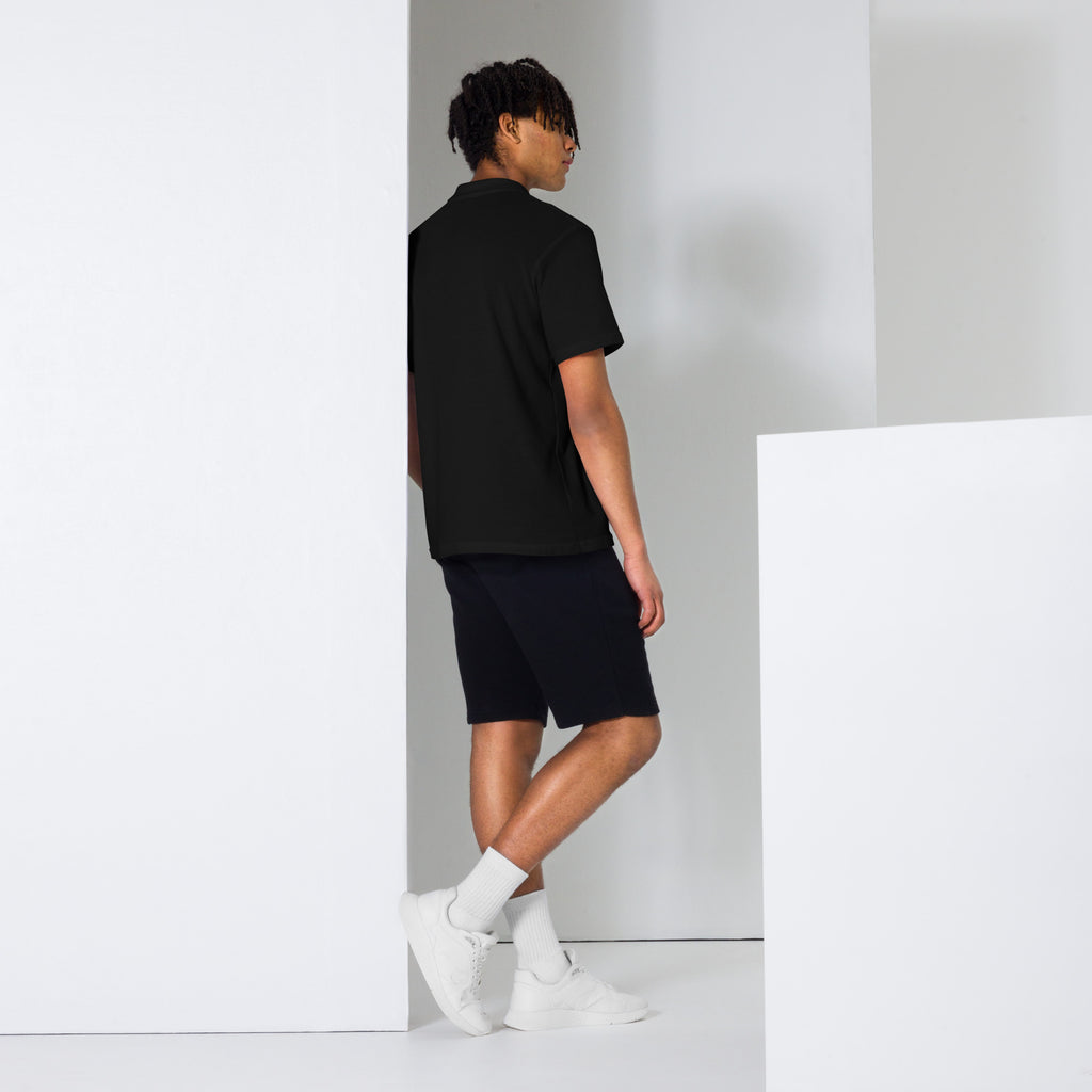 Person wearing a black t-shirt and shorts standing against a white wall.