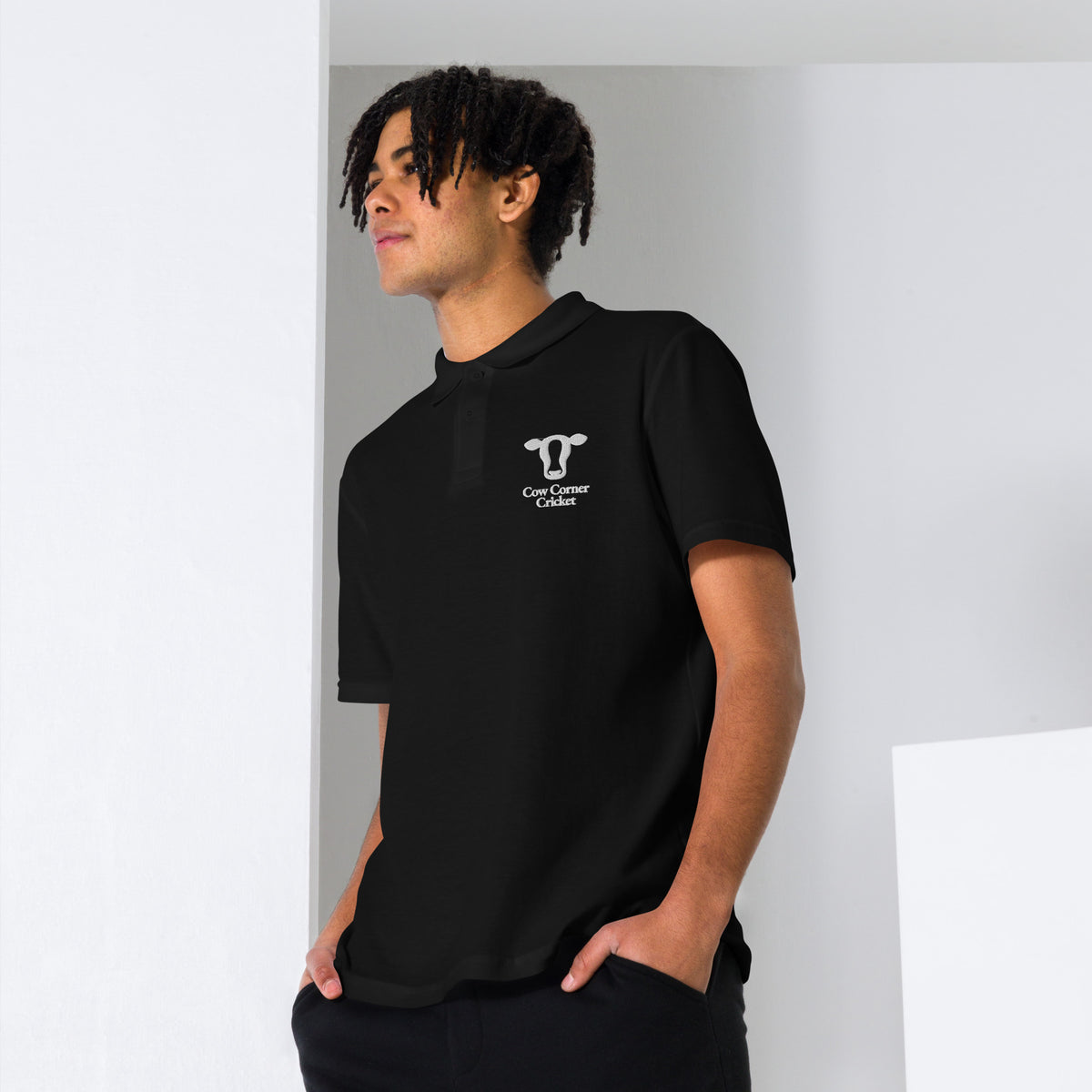 Person wearing a black polo shirt with a cow corner cricket logo on a plain background