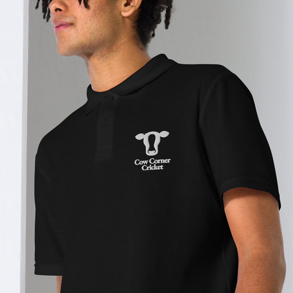 Person wearing a navy blue polo shirt with a cow corner cricket logo on chest