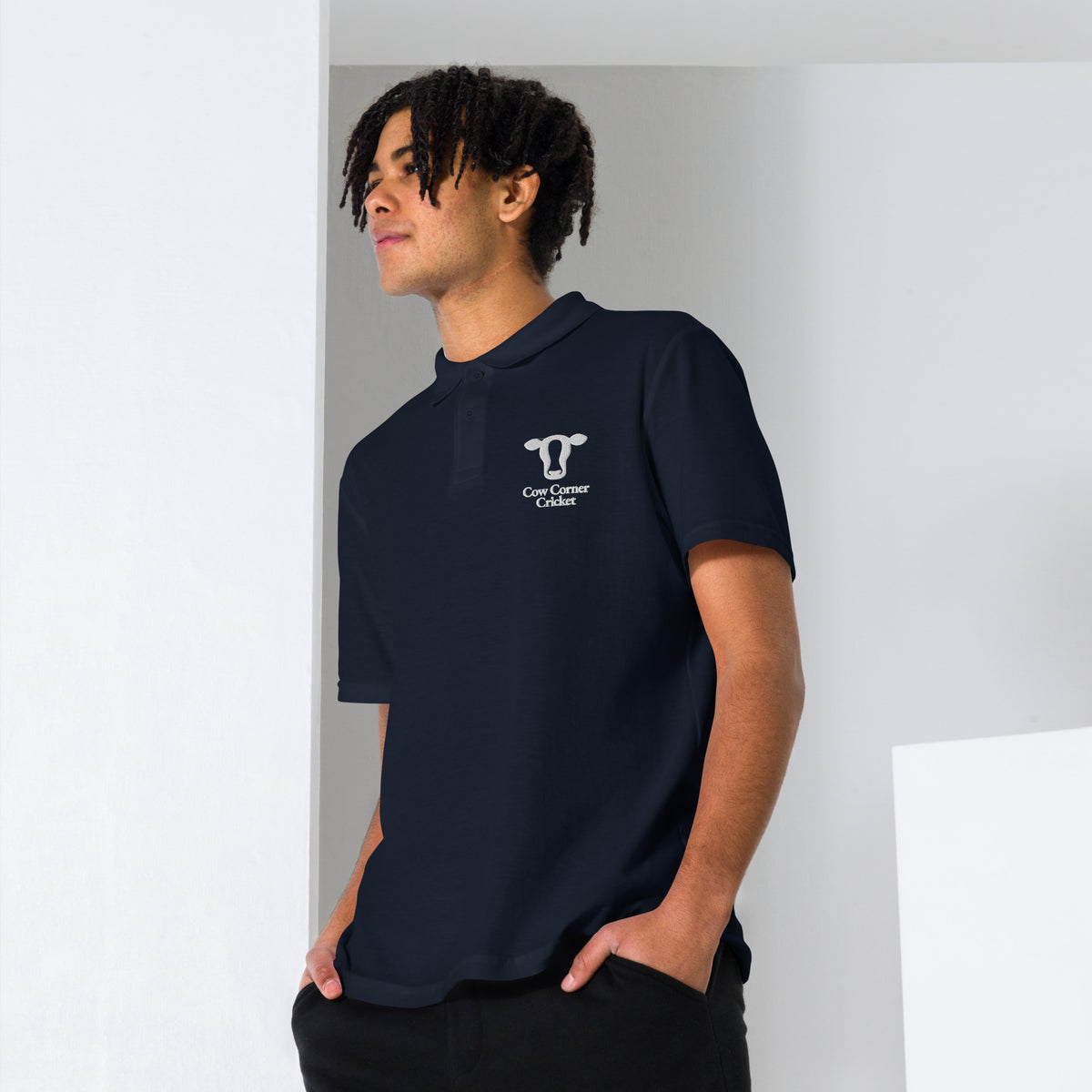 A man wearing a dark navy polo shirt with Cow Corner Cricket logo on the chest