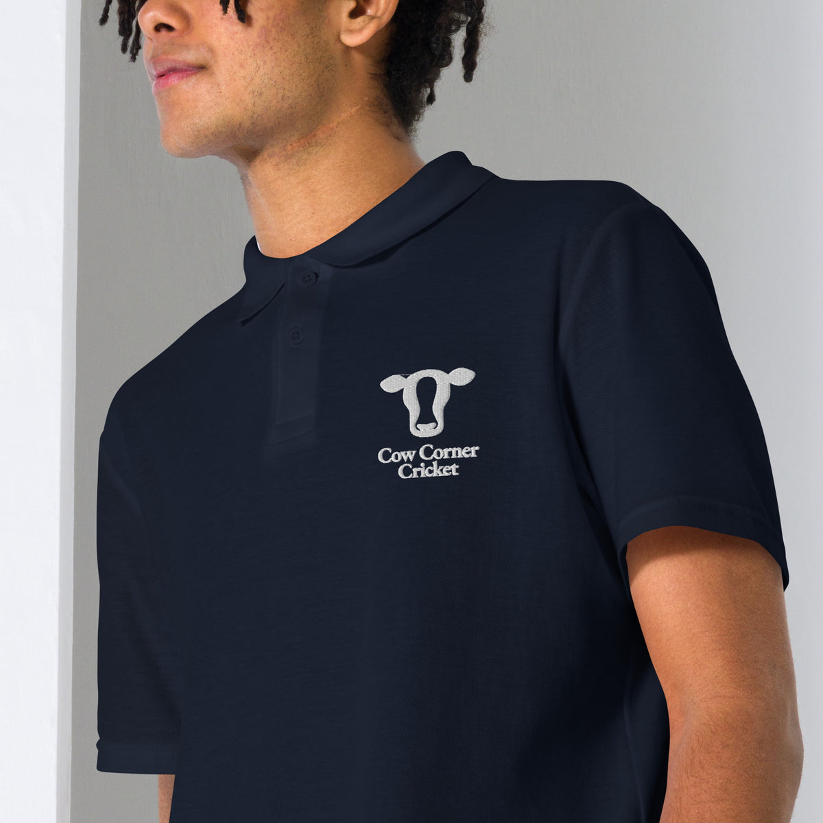 Person wearing a navy blue polo shirt with a Cow corner cricket logo on chest