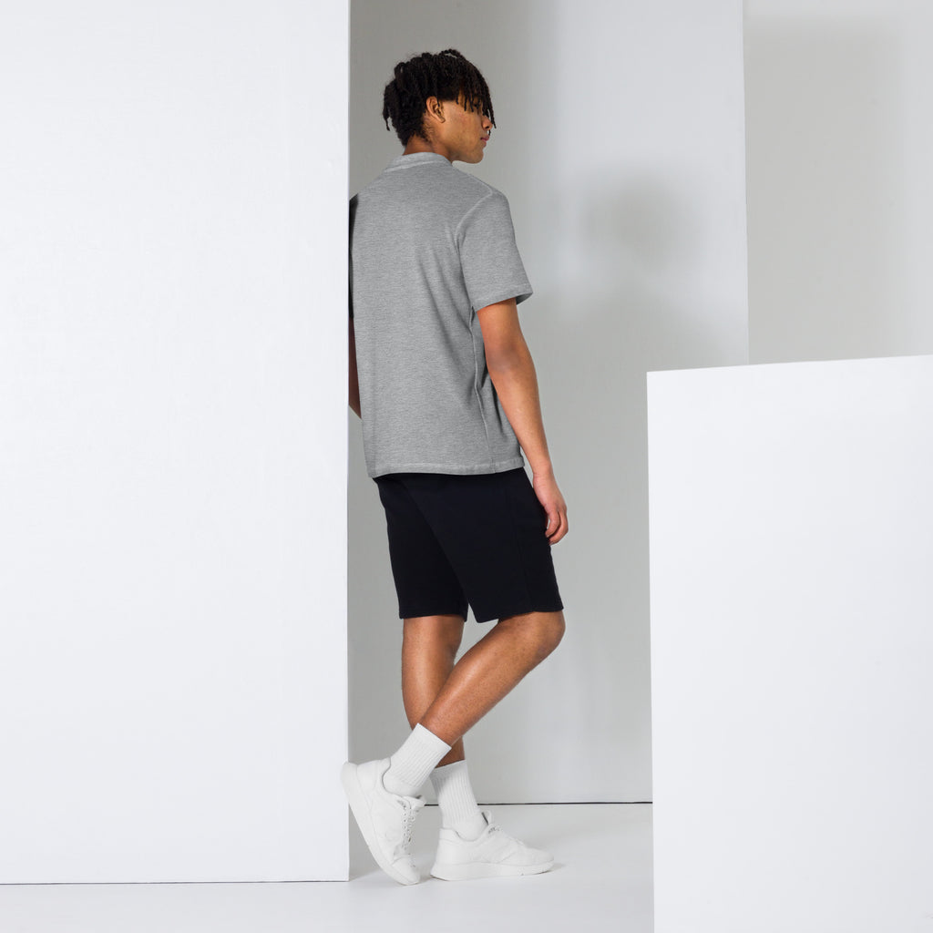 Person wearing a gray t-shirt and black shorts standing against a white wall.