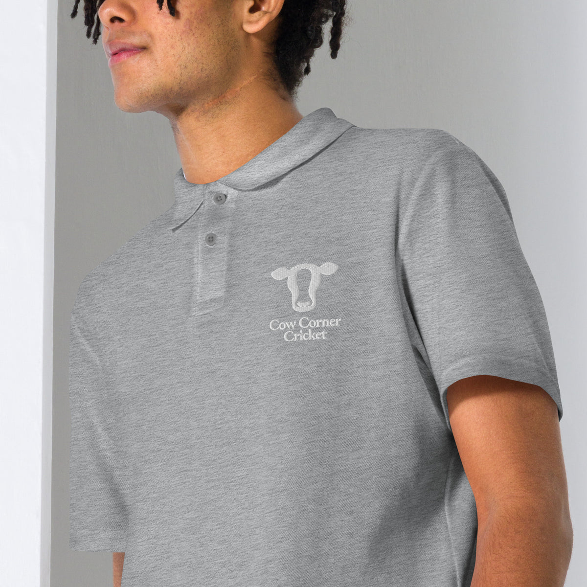 A man wearing a heather gray short-sleeve polo shirt with Cow Corner Cricket logo on the chest