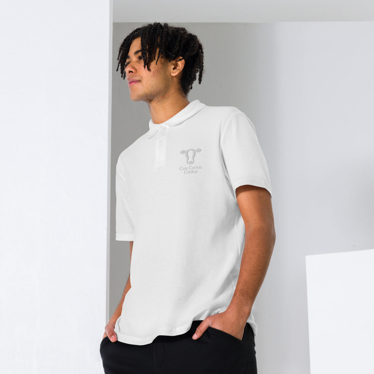 Person wearing a white polo shirt with a Cow corner cricket logo on chest